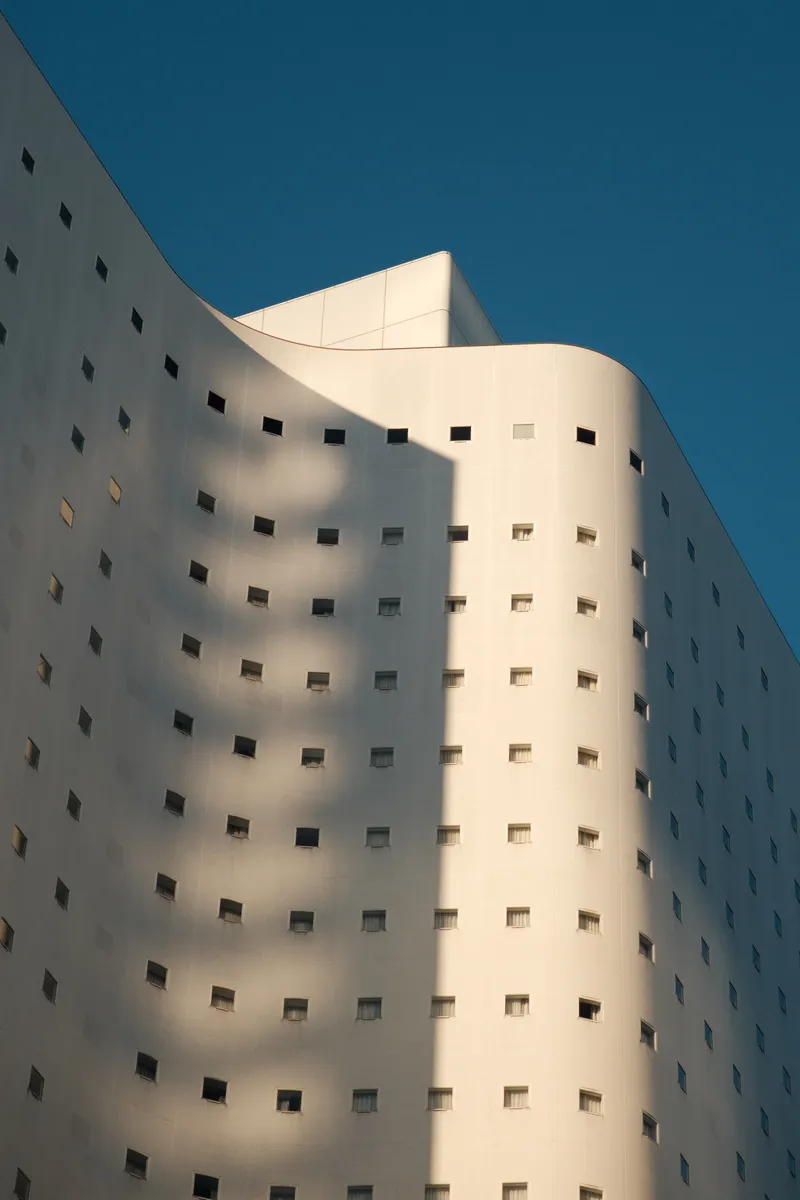 Curved white building facade with rows of small square windows against a clear blue sky