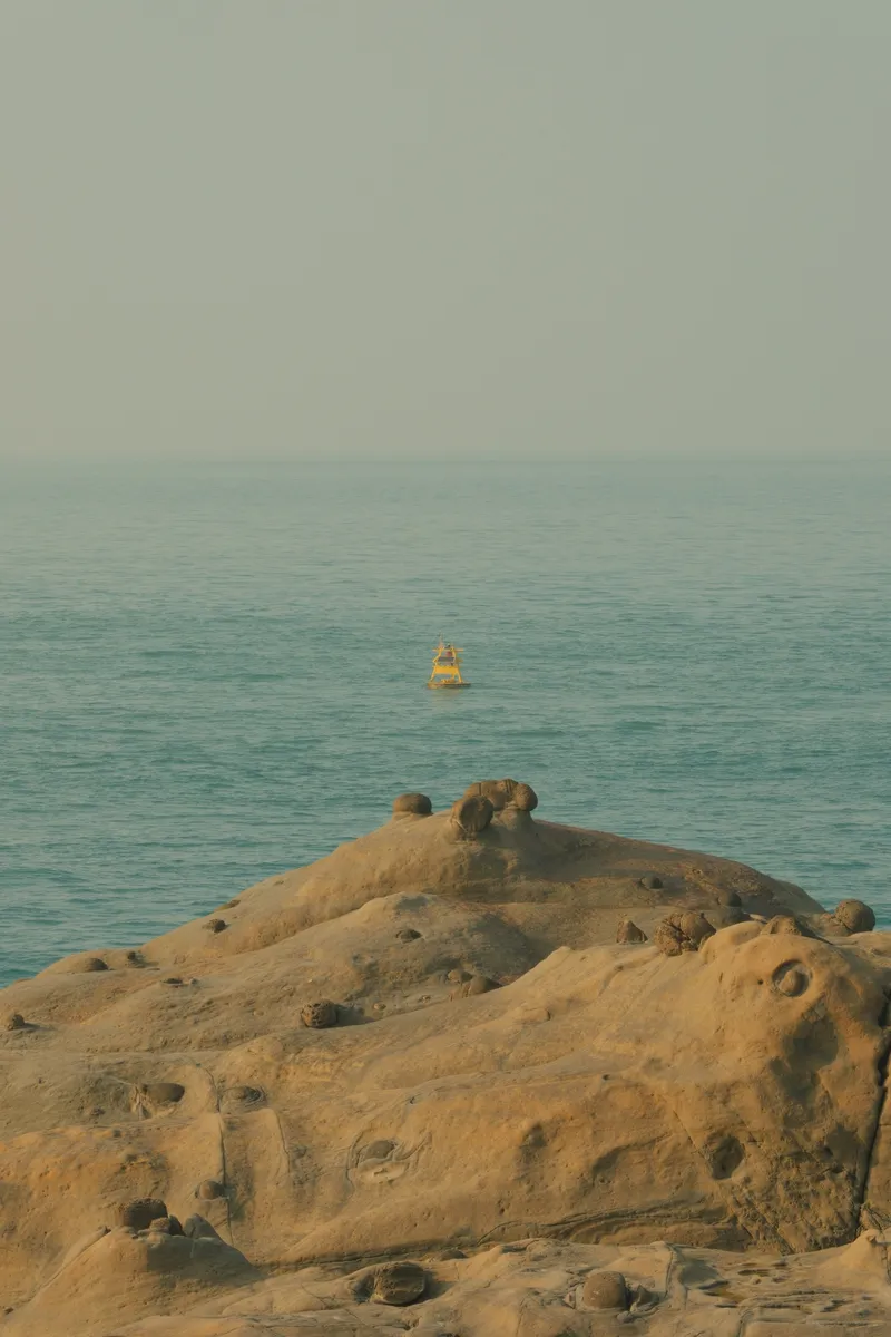 Weathered sandstone rock formations with a yellow buoy on the horizon