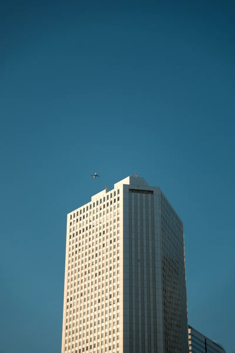 Sunlit skyscraper tower with a plane passing overhead against deep blue sky