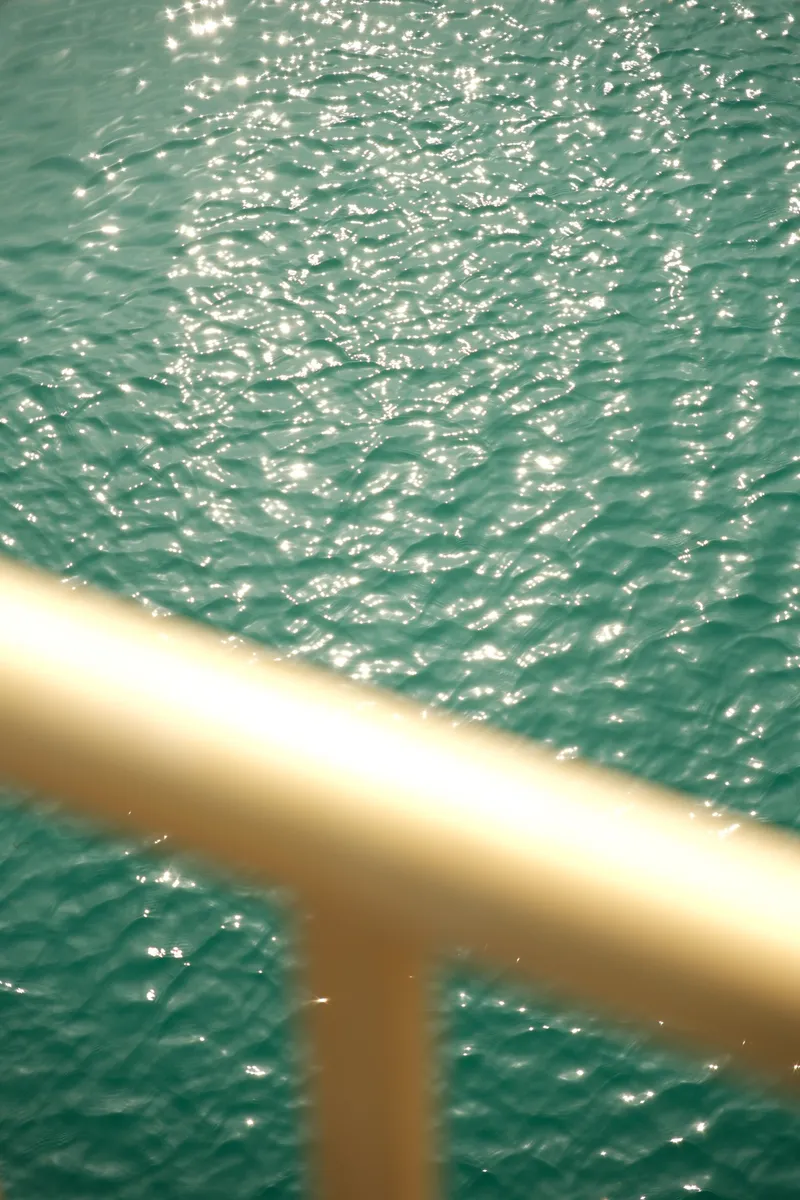 Sunlight sparkling on turquoise harbor water seen through a railing